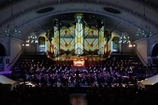 The Philharmonia playing on a dark stage, illuminated by lights projected on an organ