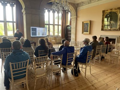 Sam Hirst delivering a presentation to an audience inside a grand room at Newstead House.