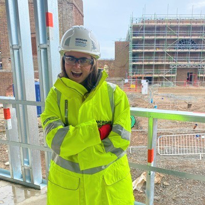 Emma Sharman smiling and wearing a yellow high-vis jacket, standing on a building site