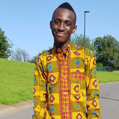 Francis Adam standing outside, wearing a patterned shirt and smiling to the camera