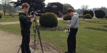 Two students stand in a field, filming their field work.