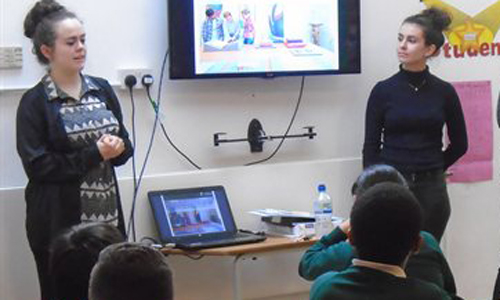 Two students delivering a presentation for primary school students in a classroom