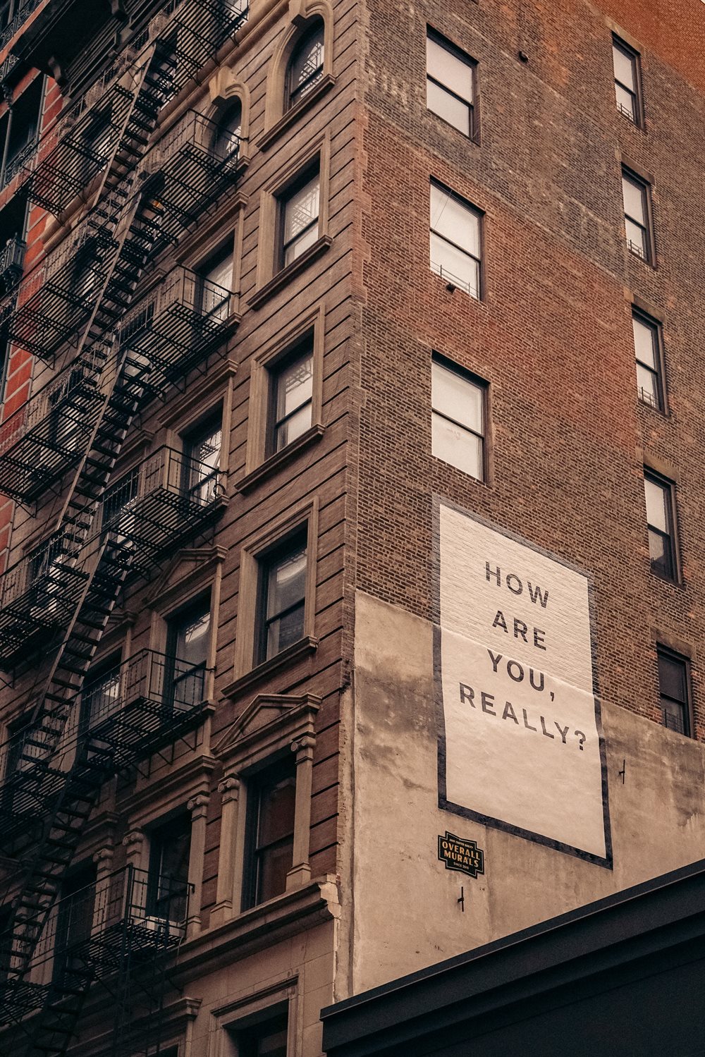 Corner of a multi-story building with a sign which reads "How are you really?"