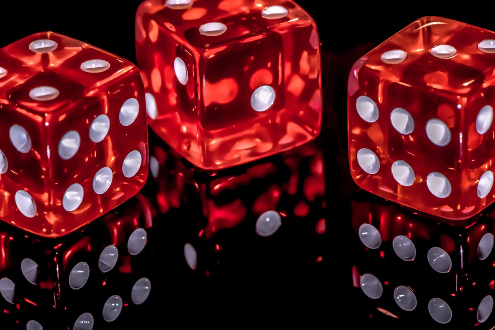 Three red dice with white spots on a black reflective surface