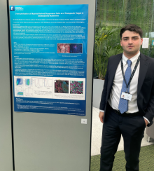 Photo of Daniele Scotto standing next to a poster displaying his research