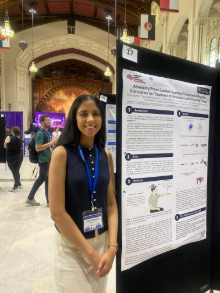 Photo of Priya Sharma at a conference standing next to a poster displaying her research