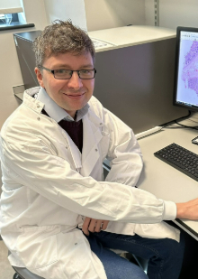 Photo of William Dalleywater wearing a lab coat, sitting at a desk using a computer