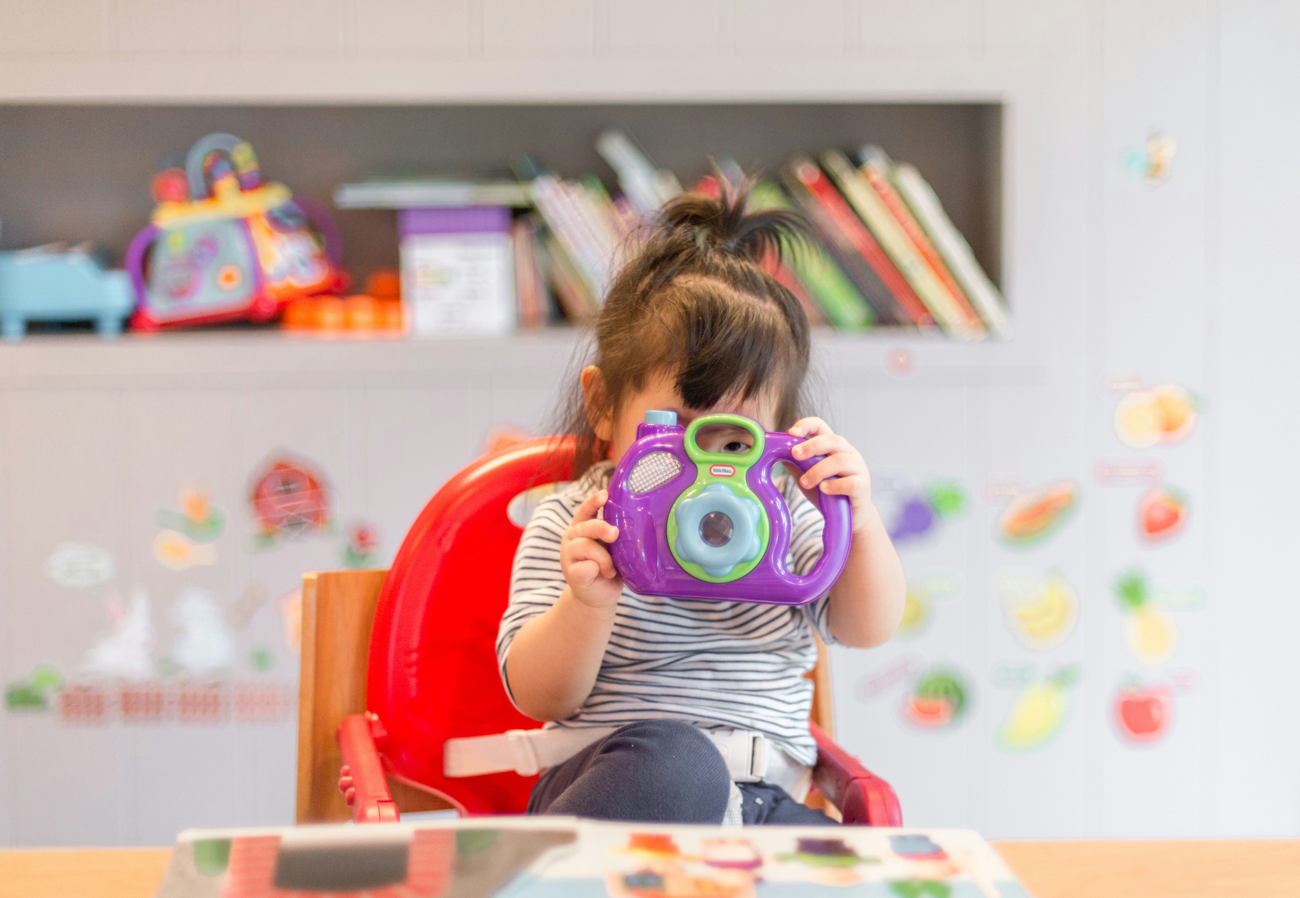 Camera child sat on a red chair holding a purple plastic camera