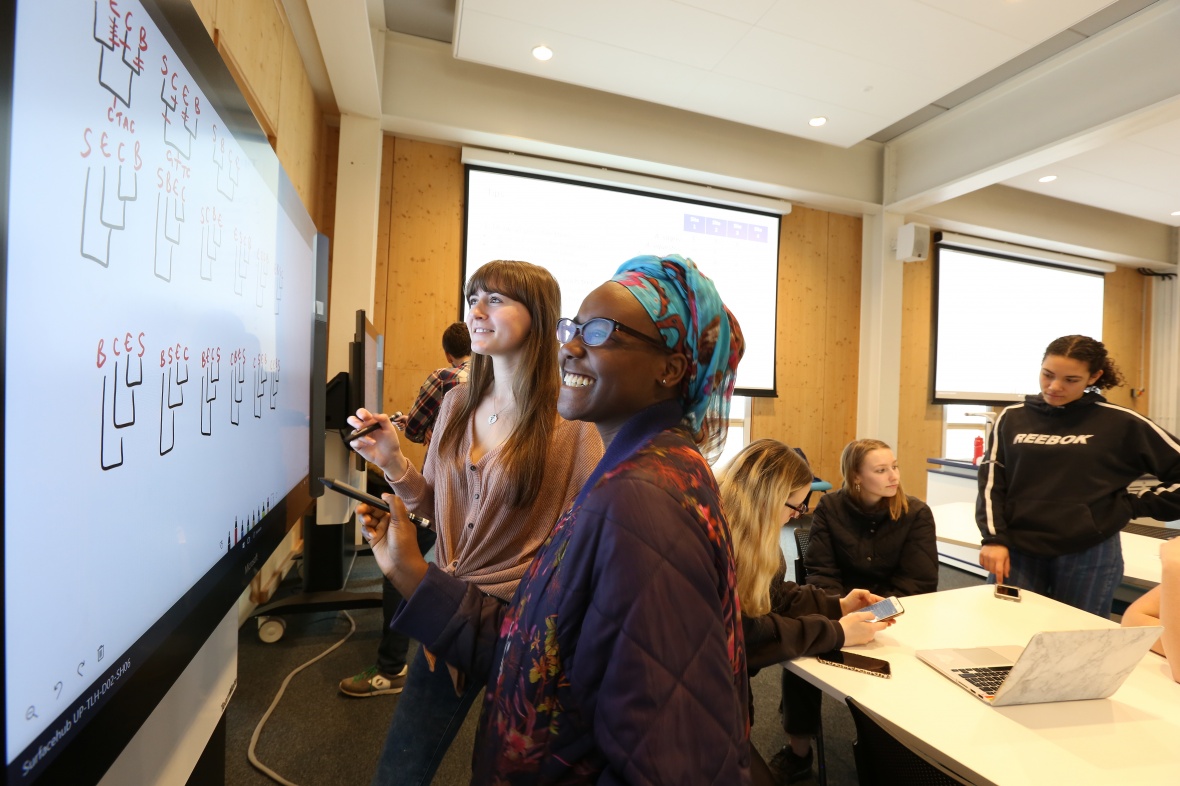 Two smiling undergraduate students write maths problems on a digital whiteboard