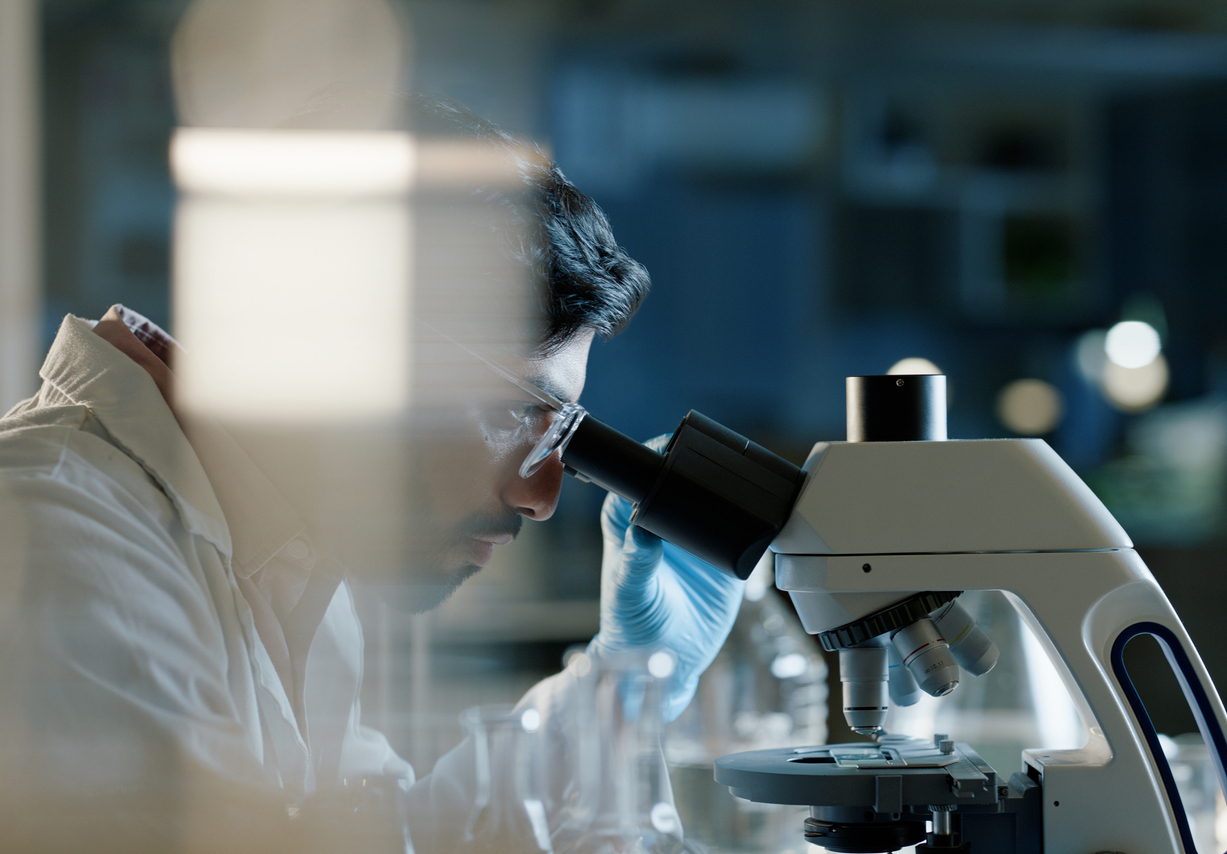 man looking into a microscope with goggles on