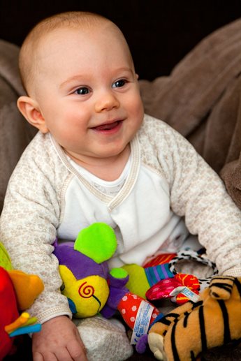 A baby wearing a white and patterned babygrow playing with toys, laughing