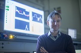 Image of Prof Mark Sumner, academic in PEMC. Standing in front of a screen showing graphs and research simulations