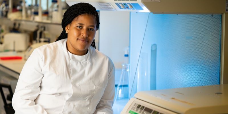 Head and shoulders portrait of researcher in white lab coat with equipment in background