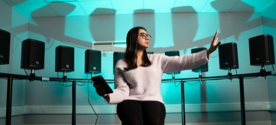 Person sitting in middle of circle of speakers holding ipad with arm outstretched