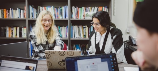 Researchers working on laptops in front of bookshelves, smiling