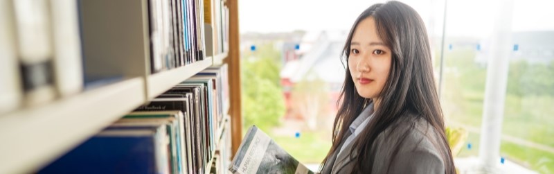 Student in front of bookshelves holding books in arms