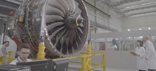 Engineers looking up at large jet engine in factory