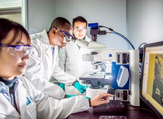 Three researchers in white coats working in lab