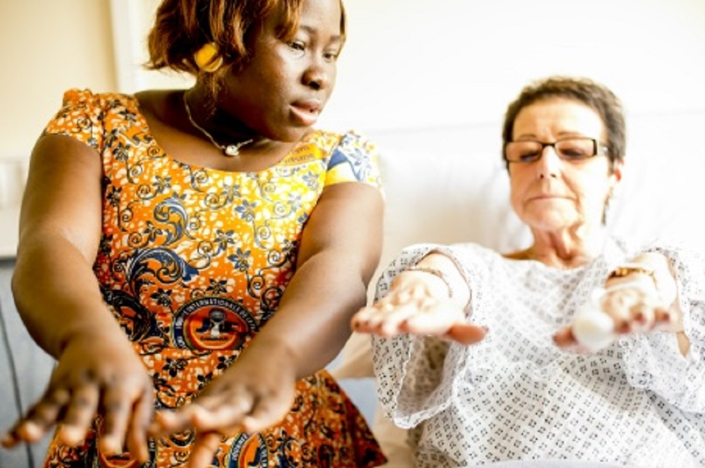 on the left is a woman in yellow dress holding out her arms with a female patient wearing a gown on the right also holding out her arms following exercises