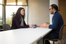 A man and woman sitting opposite each other at a table with notepads and folders on it having a discussion