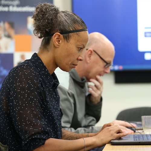 A man and a woman work on laptops during a training programme.