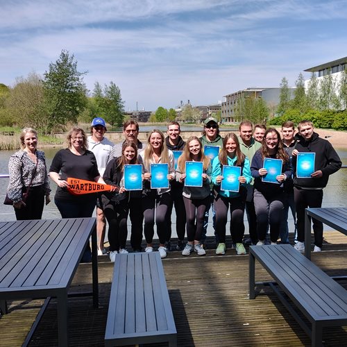 Group photo of Wartburg college students and staff holding participation certificates in front of Jubilee lake.