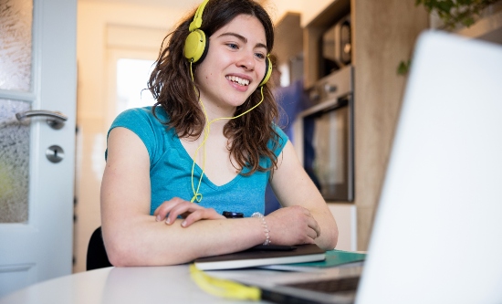 A student with headphones talking online using her laptop