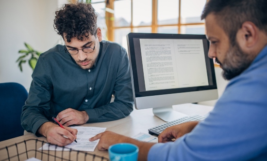 Two men reviewing a document with one man pointing at the text and the other man making amends with a pen