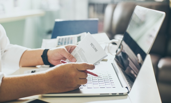 A man reading his printed resume or CV in front of a laptop