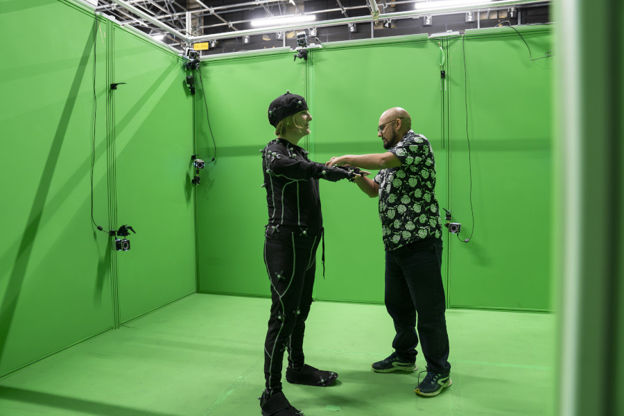 Green screen room with person wearing motion caption suit being fitted by someone else