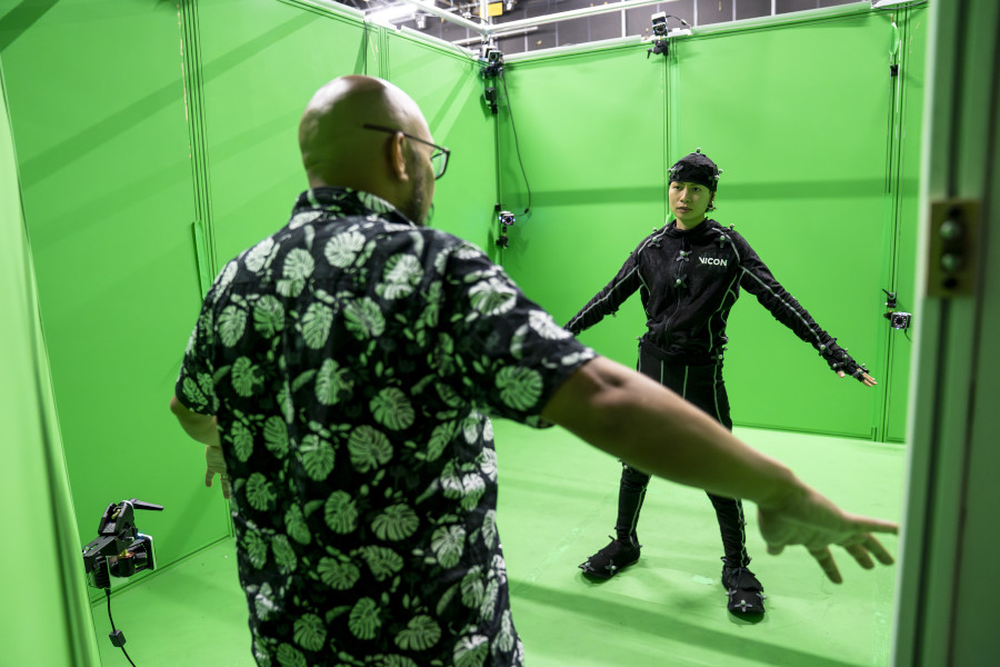 Green screen studio with two people facing each other mirroring their movements with one wearing a motion capture suit