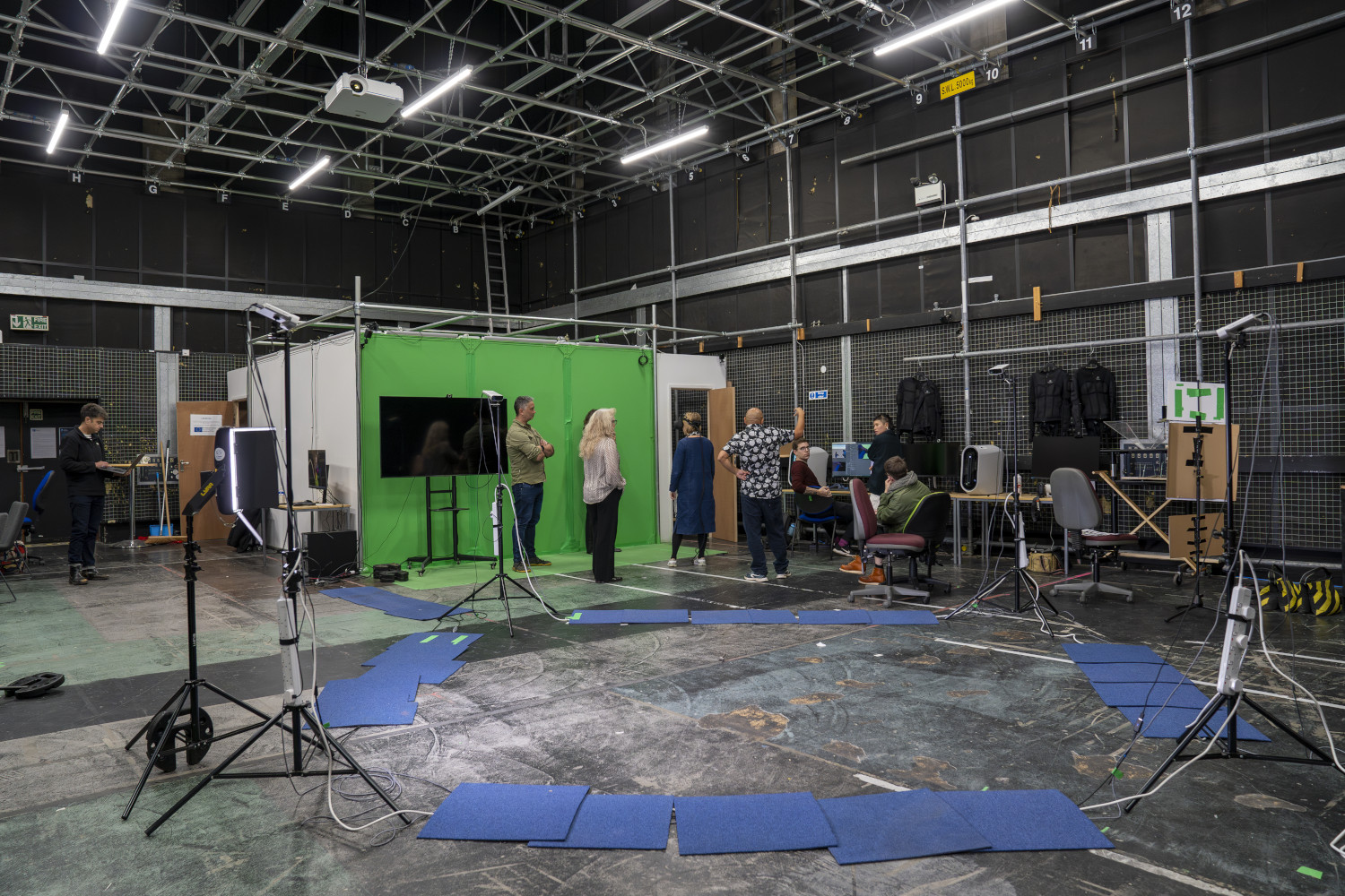 Film production studio with five people standing and chatting and three people sat down