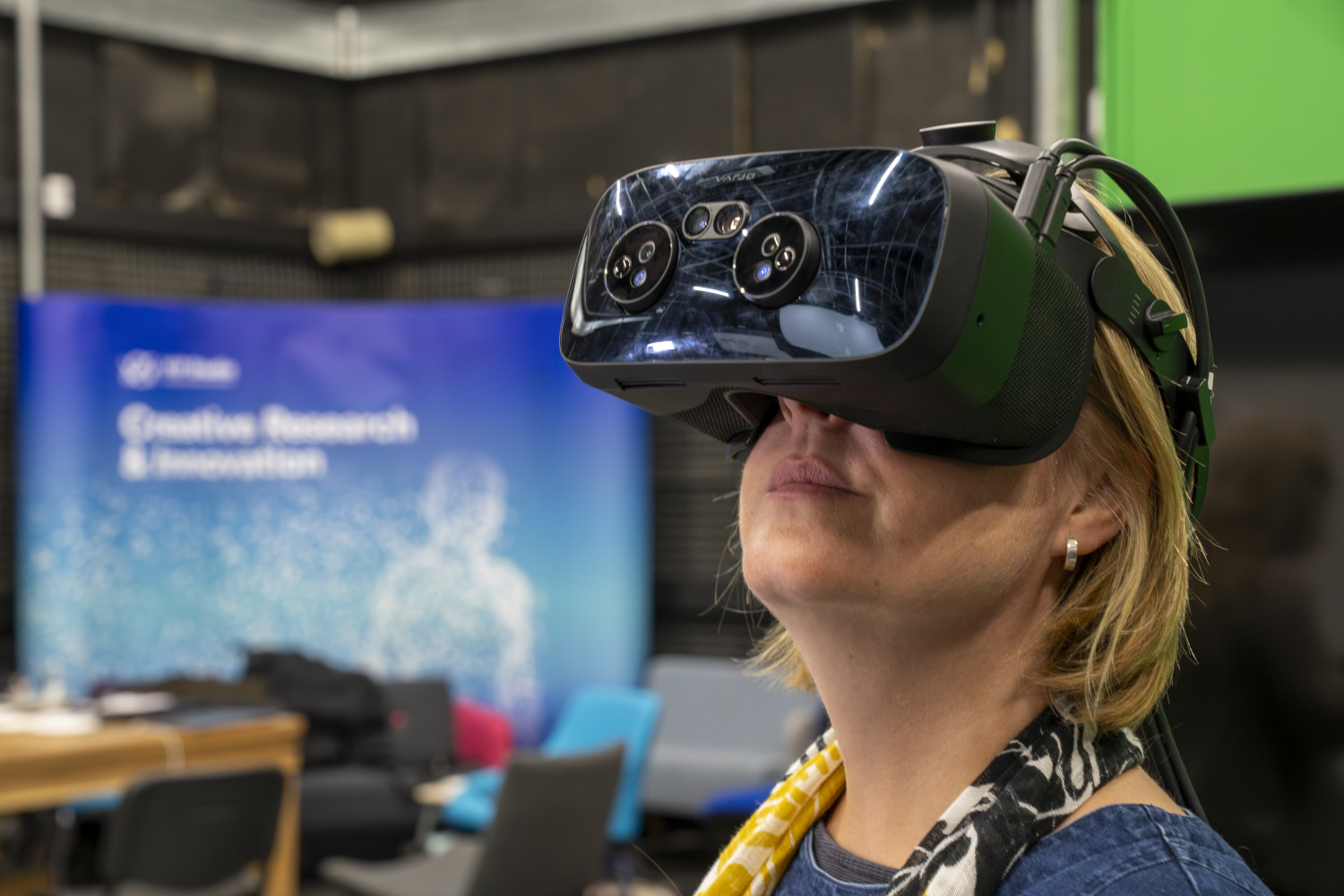 Woman wearing a vr headset with banner in the background that says ‘creative research and innovation’