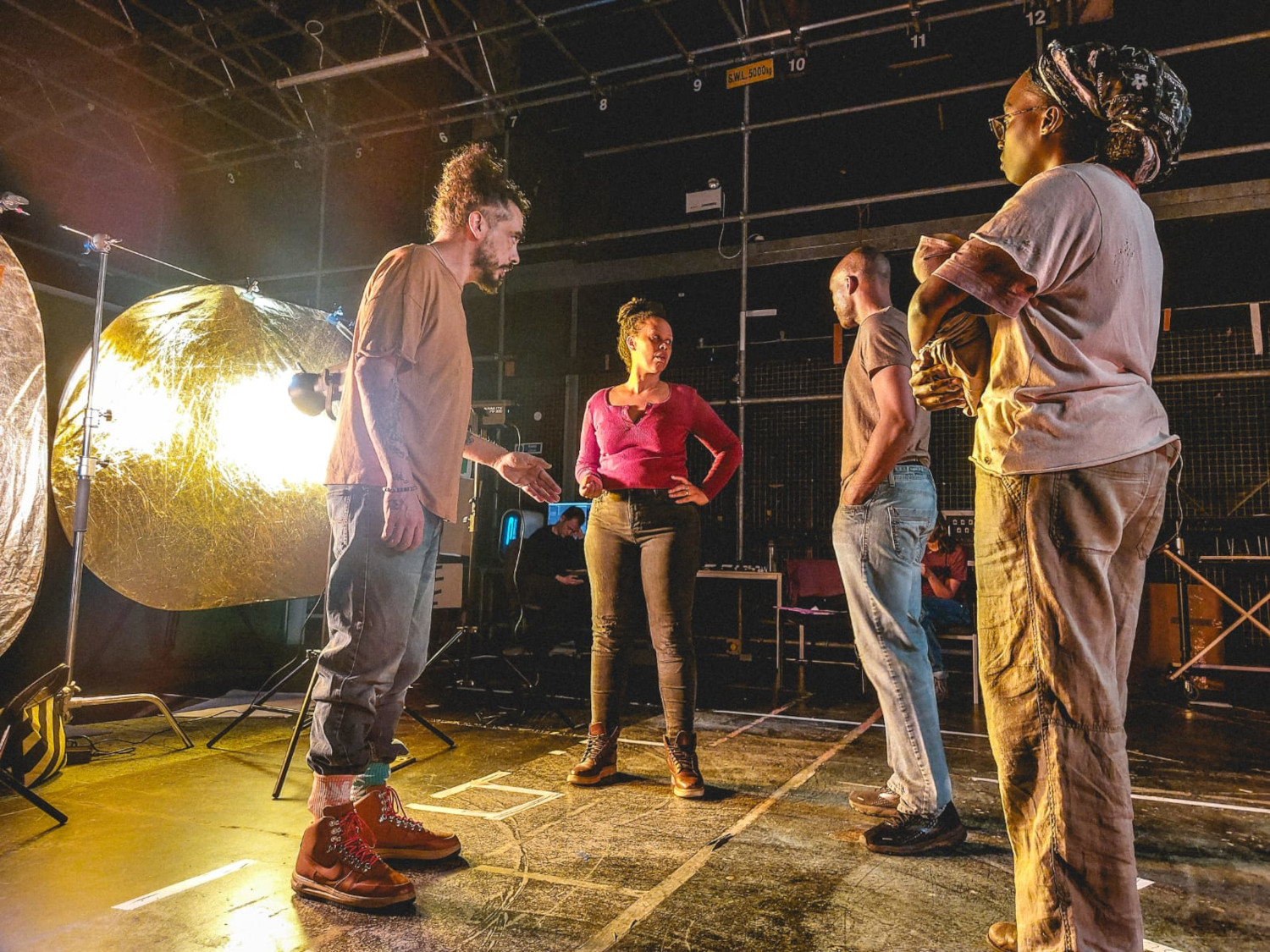 Four people standing in a circle. They are stood in a film production studio with a bright light behind them