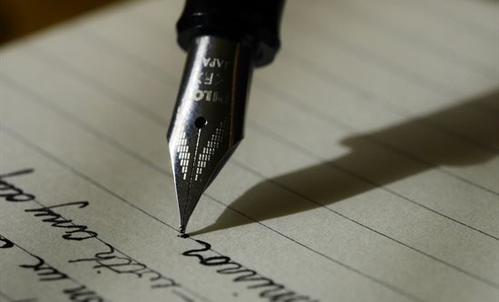 Image of a fountain pen writing text on a piece of ruled paper.