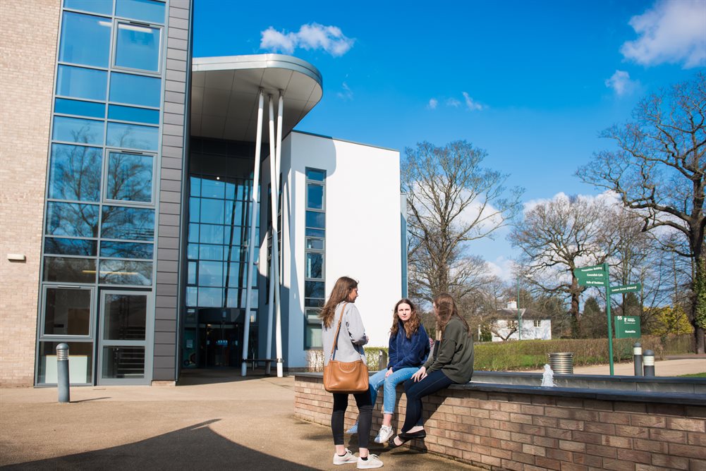 Outside of the Humanities building with three students sitting in-front