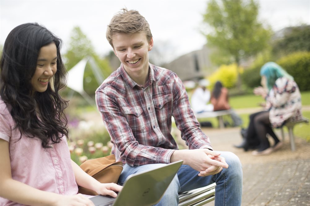 Two students looking at laptop outdoors, smiling