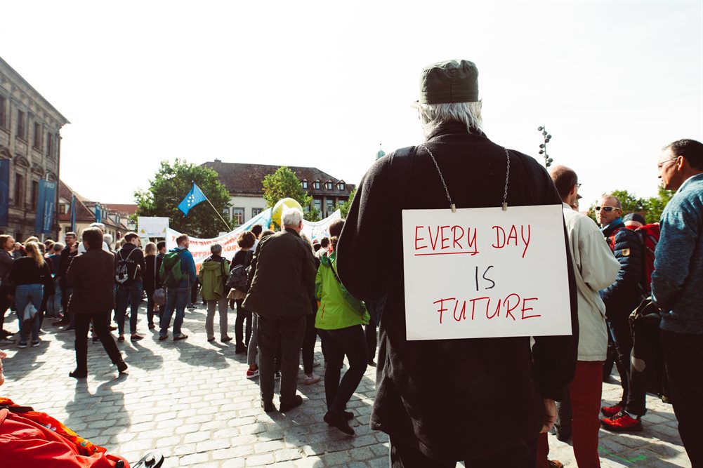 Older man stood in a crowd wearing a banner which reads every day is future