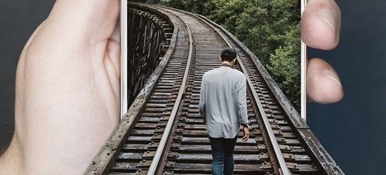 A man walking along a train track into a smartphone screen, which is being held by a hand