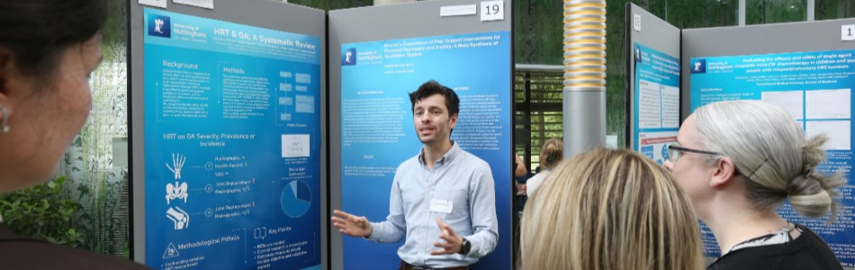 An academic presenting their research poster with three women watching.