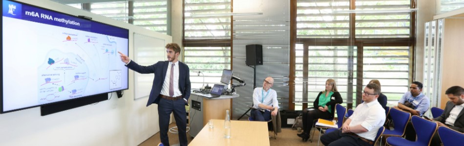 An academic pointing at their research on a screen with observers sitting watching.