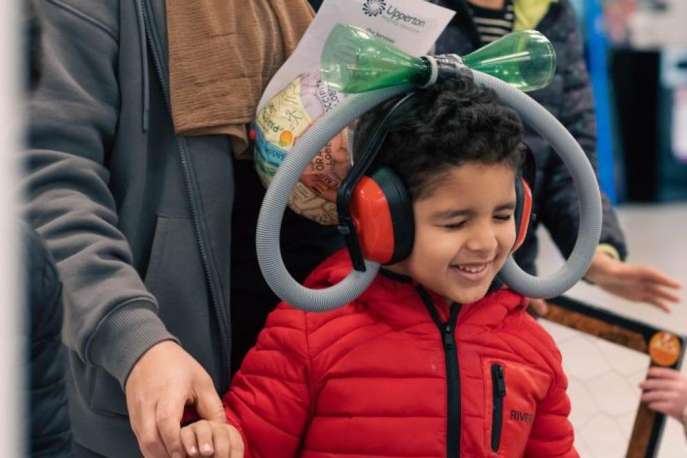 A young boy trying a sound experiment wearing red ear defenders.