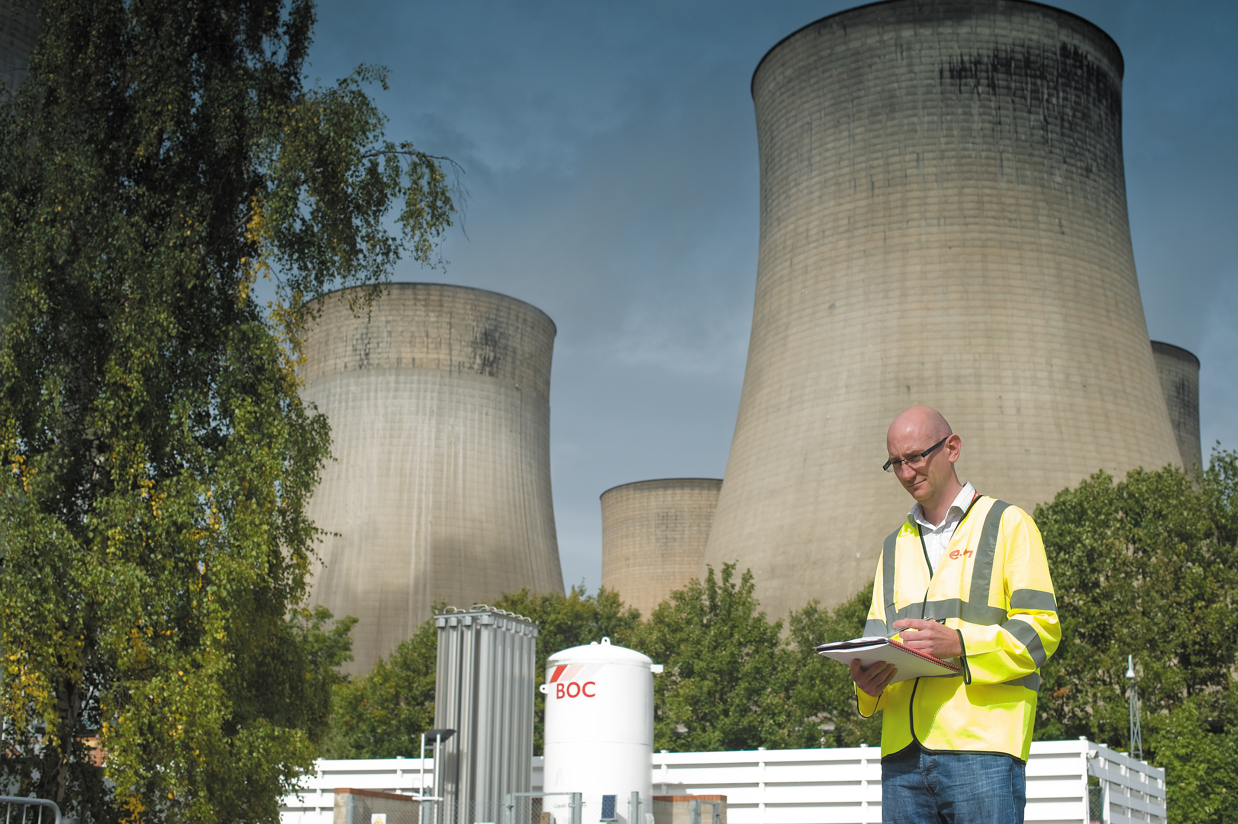 A white male worker standing in front of a huge industrial building