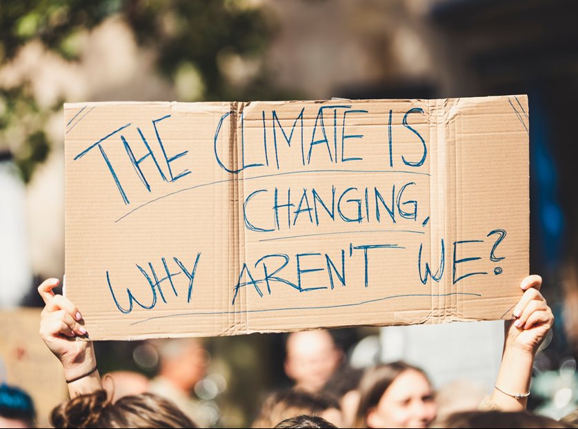 Hands holding cardboard placard saying 'The climate is changing, why aren't we?' 