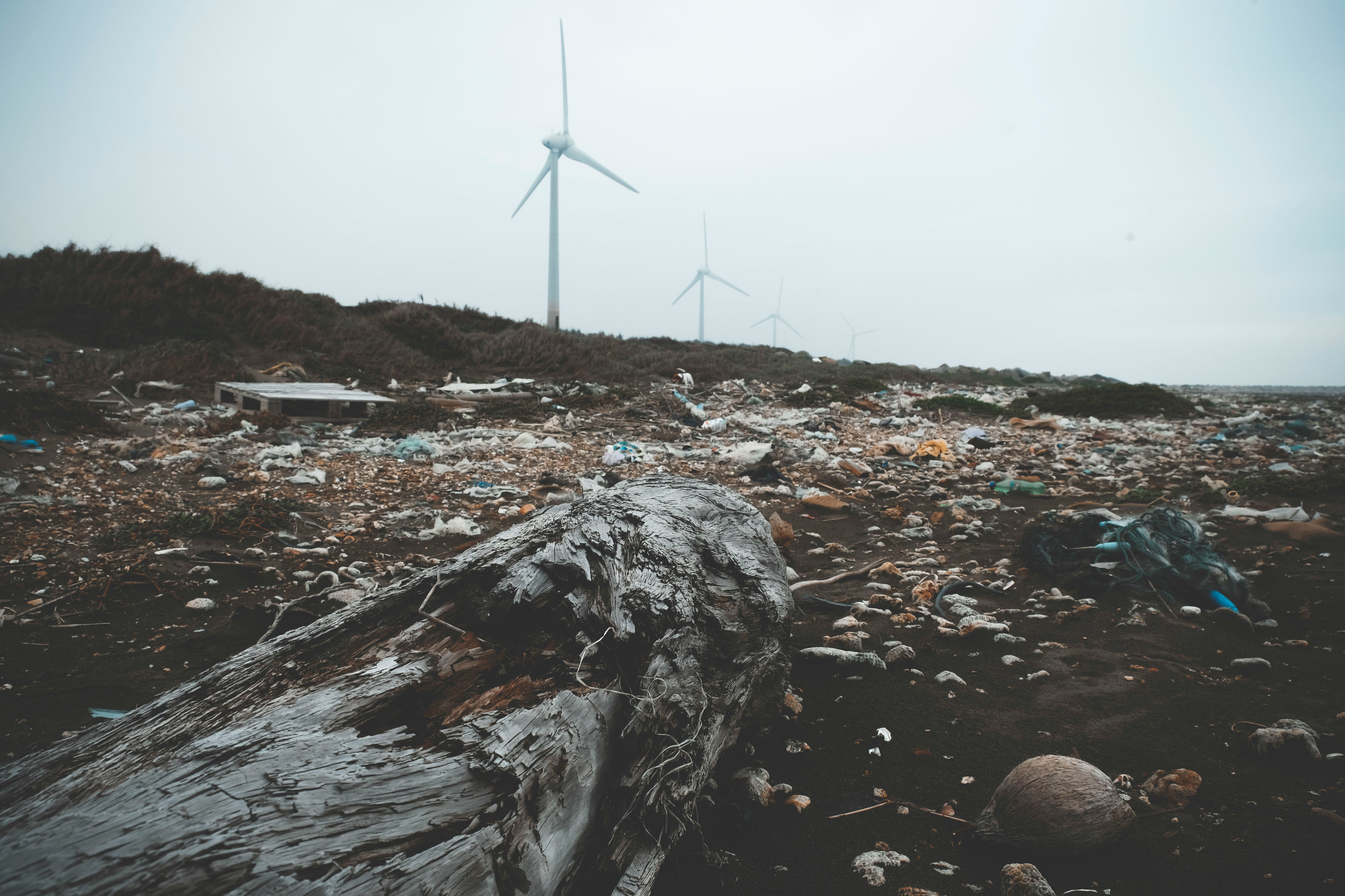 A landscape with wind turbines in the background and a foreground littered with various pieces of trash