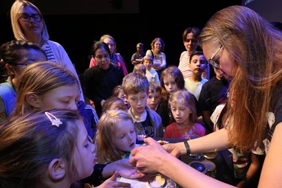 Children and adults crowd round a presenter looking at something hidden in her hands