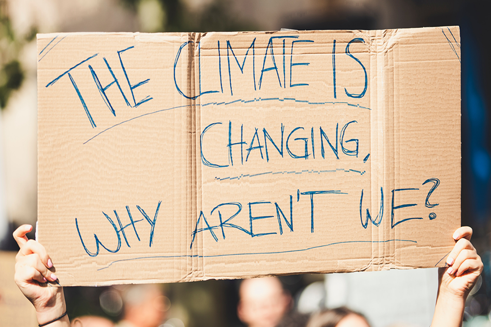 Hands holding cardboard placard saying 'The climate is changing, why aren't we?'