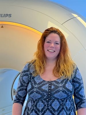 Rebecca Dewey standing in front of an MRI scanner, smiling