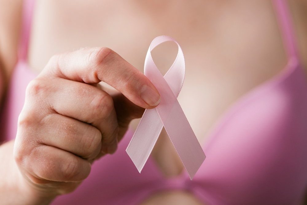 A person in a pink bra holding a pink awareness ribbon