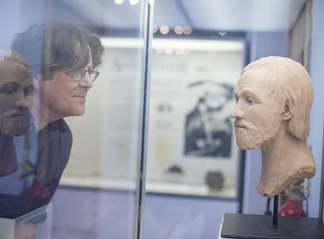 Side shot of a man's face and a sculpted bust inside a glass case facing each other
